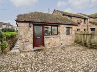 A stone building with a door and windows with a paved area and wooden fence at Ramblers Rest in St Just