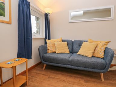 A sitting area with a blue sofa with yellow cushions a floor lamp a window with blue curtains and a small orange side table