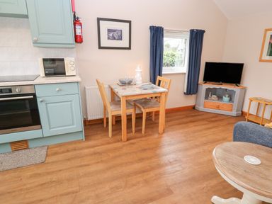A kitchen and dining area with a table and two chairs a microwave oven a television on a stand and a window with curtains at Ramblers Rest in St Just