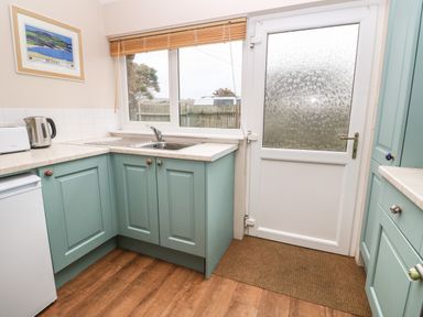 A kitchen with a sink under a window a glass door and green cabinets at Ramblers Rest in St Just