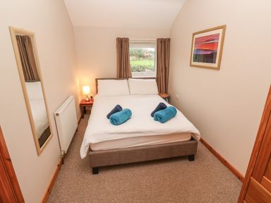 A bedroom with a double bed two rolled towels bedside tables table lamp window mirror and a framed picture at Ramblers Rest in St Just