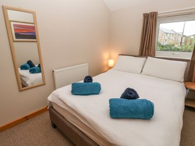 A bedroom with a double bed with white linens and blue towels on top a wooden framed mirror radiator and a window with brown curtains at Ramblers Rest in St Just