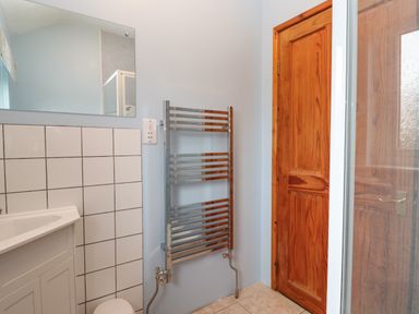 A bathroom with a white tiled wall, a wall-mounted towel radiator, a wooden door, and a mirror above a sink at Ramblers Rest in St Just