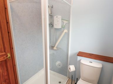 A bathroom with a shower enclosure and a toilet with a wooden shelf above at Ramblers Rest in St Just