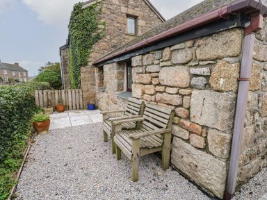 Two wooden chairs on a gravel patio beside a stone house with plants in pots and a wooden fence at Ramblers Rest in St Just