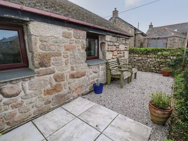 An outdoor stone patio area with a wooden bench gravel ground and potted plants at Ramblers Rest in St Just