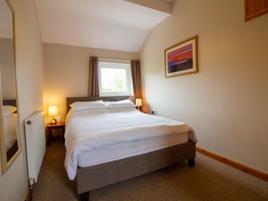 A bedroom with a double bed two bedside lamps a window with curtains and a framed picture on the wall at Ramblers Rest in St Just