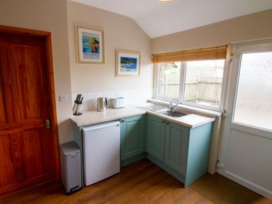 A kitchen with teal cabinets a sink a mini fridge a kettle toaster knife block and framed pictures at Ramblers Rest in St Just