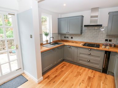 A kitchen with grey cabinets wooden countertops a gas stove and a sink next to a window at Rose Cottage in Bishopsteignton