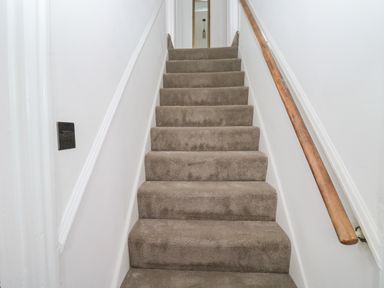 A carpeted staircase with a wooden handrail on the right and white walls at Rose Cottage in Bishopsteignton