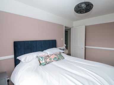 A bedroom with a bed with white bedding and a decorative pillow and a blue headboard at Rose Cottage in Bishopsteignton
