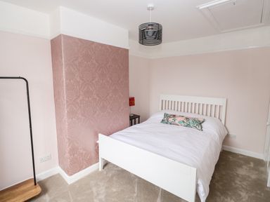 A bedroom with a white bed and floral cushion next to a patterned wall at Rose Cottage in Bishopsteignton