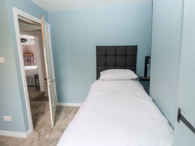 A small bedroom with a single bed against a blue wall and an open door showing another room at Rose Cottage in Bishopsteignton