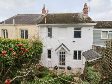 Rear exterior of a two story white house with a small garden and tiled patio at Rose Cottage in Bishopsteignton