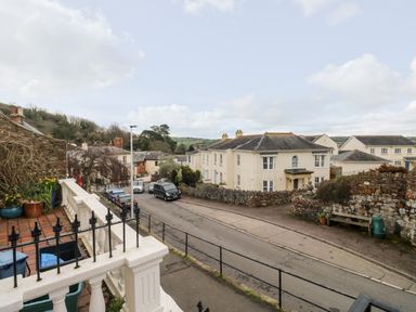 A street view with parked cars and stone walls beside residential buildings at Rose Cottage in Bishopsteignton