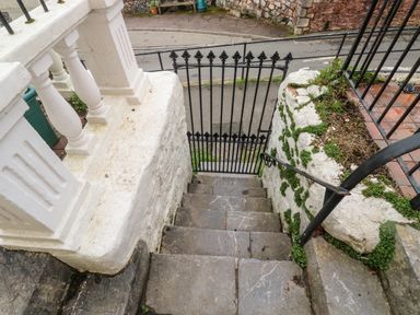 Stone steps leading down to a black wrought iron gate with white stone walls and greenery on the side