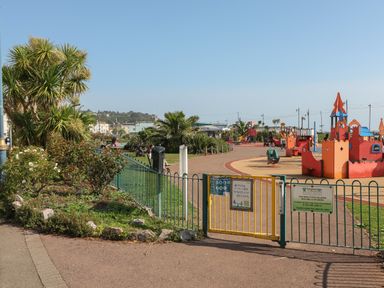 A fenced playground with colorful play structures and plants along a pathway at Rose Cottage in Bishopsteignton