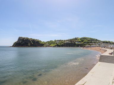 A beach with a concrete walkway and steps next to a bay with hills and houses in the background at Rose Cottage in Bishopsteignton
