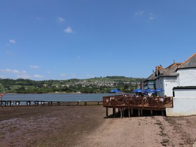 A riverside view with a wooden deck and umbrellas at Coombe Cellars pub and restaurant in Bishopsteignton