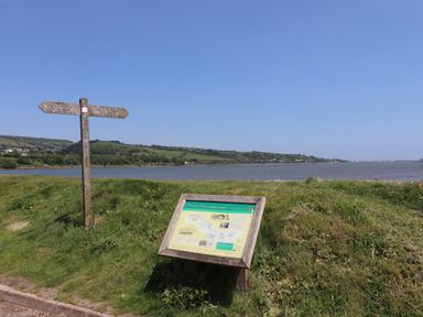 A riverside with a wooden signpost and an information board in a grassy area at Rose Cottage in Bishopsteignton