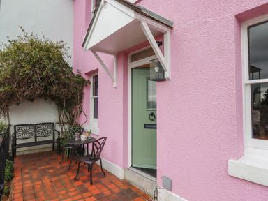 An outdoor patio with a green door and a pink wall with a small table and chairs at Rose Cottage in Bishopsteignton