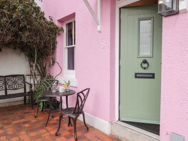 An outdoor patio with a small metal table and chairs next to a pink wall and green door at Rose Cottage in Bishopsteignton