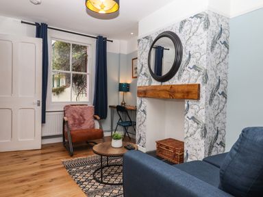 A living room with a fireplace a round mirror blue curtains and a chair at Rose Cottage in Bishopsteignton