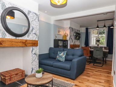 A living room with a blue sofa a round wooden coffee table and a dining area with chairs at Rose Cottage in Bishopsteignton