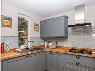 A kitchen with grey cabinets wooden countertops a gas stove a double sink and a window with plants outside at Rose Cottage in Bishopsteignton