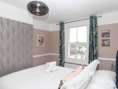 A bedroom with a bed with white linens towels on the bed patterned curtains a window and wall art at Rose Cottage in Bishopsteignton
