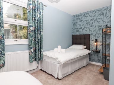 A bedroom with a single bed next to a window with curtains and animal patterned wallpaper at Rose Cottage in Bishopsteignton
