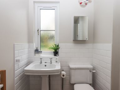 A bathroom with a pedestal sink toilet white tiles and a window with a plant on the sill at Rose Cottage in Bishopsteignton