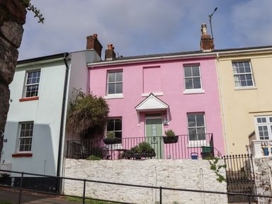 A row of three terraced houses with pastel pink yellow and blue exteriors with front doors and windows at Rose Cottage in Bishopsteignton