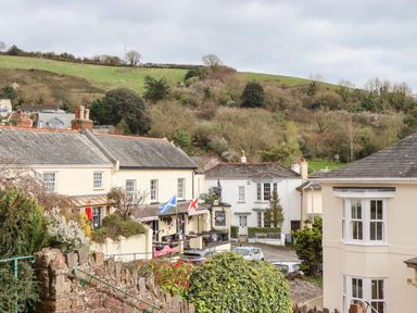 A street view with houses cars and greenery on a hillside at Rose Cottage in Bishopsteignton