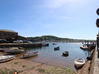 A harbor with small boats docked and floating on water near buildings and a hill in the background at Rose Cottage in Bishopsteignton