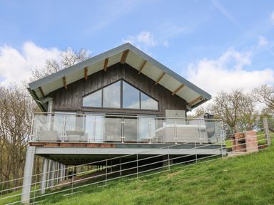 A chalet-style house with a glass-railed balcony on a grassy hillside at Barcud Coch - Red Kite in Garthmyl