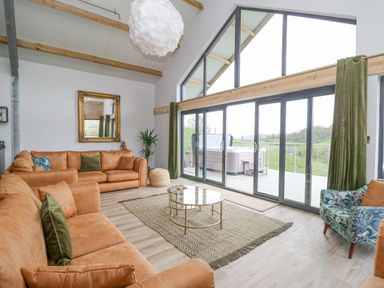 A living room with large windows a glass coffee table and brown sofas at Barcud Coch - Red Kite in Garthmyl