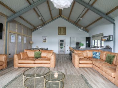 A living room with tan leather sofas a dining table and a kitchen area at Barcud Coch - Red Kite in Garthmyl