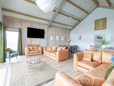 A sitting area with leather sofas a glass coffee table a TV and a dining table at Barcud Coch - Red Kite in Garthmyl