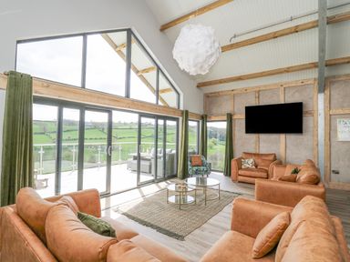 A living room with leather sofas a patterned armchair a rug and glass doors overlooking a balcony and green fields at Barcud Coch - Red Kite in Garthmyl