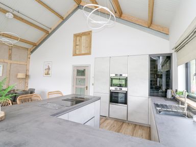 A modern kitchen with a countertop, built in ovens, sink, and dining chairs at Barcud Coch - Red Kite in Garthmyl