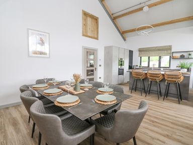 A dining area with a table set for eight and a kitchen with a breakfast bar and three stools at Barcud Coch - Red Kite in Garthmyl
