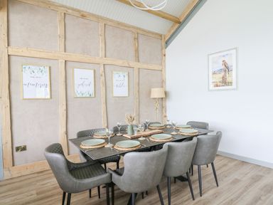 A dining room with a table set for eight and framed artwork on the walls at Barcud Coch - Red Kite in Garthmyl