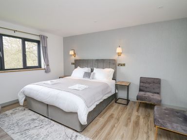 A bedroom with a double bed two bedside tables two chairs a window and wooden flooring at Barcud Coch - Red Kite in Garthmyl