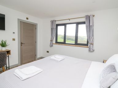 A bedroom with a bed folded towels a window with curtains a wooden door and a small desk with a chair at Barcud Coch - Red Kite in Garthmyl