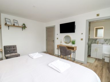 A bedroom with a bed towels on it a chair a desk with a chair and a plant a wall mounted television and an entrance to a bathroom at Barcud Coch - Red Kite in Garthmyl