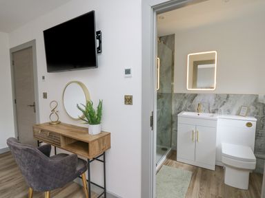 A desk with a chair and a mirror next to a bathroom with a sink vanity and toilet at Barcud Coch - Red Kite in Garthmyl
