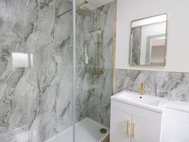 A bathroom with a shower area and a sink with a mirror above at Barcud Coch - Red Kite in Garthmyl