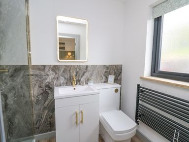 A bathroom with a white sink cabinet and toilet next to a window and a black towel radiator at Barcud Coch - Red Kite in Garthmyl