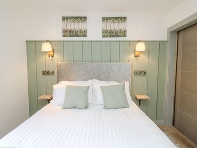 A bed with two pillows and cushions with green wooden paneling wall and two wall lamps at Barcud Coch - Red Kite in Garthmyl